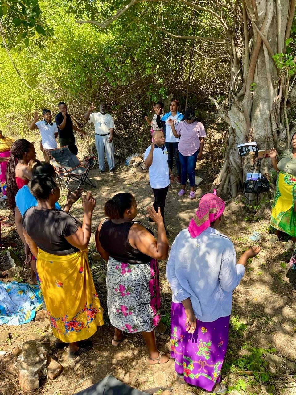 Heavenly Grace members gathered in prayer beneath a large tree outdoors
